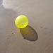 Yellow balloon cast a shadow and reflection on sand.